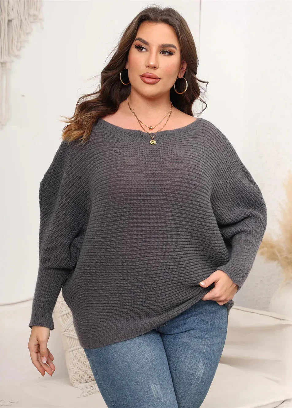 Woman wearing a gray sweater and blue jeans in a neutral setting
