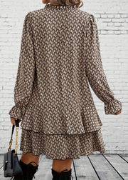 Person wearing a patterned dress with long sleeves against a white brick wall.