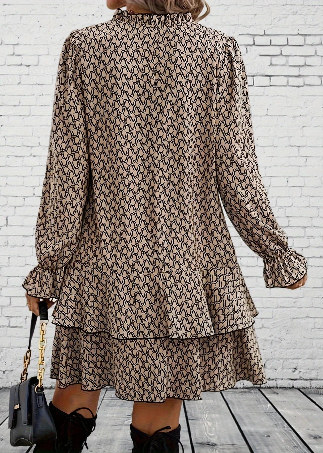 Person wearing a patterned dress with long sleeves against a white brick wall.