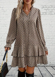 Woman wearing a patterned dress with long sleeves against a white brick wall.