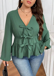Woman wearing a green peplum top with ruffles and bows, standing indoors.