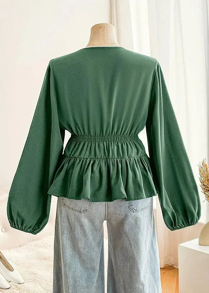 Green blouse with balloon sleeves on a mannequin against a white curtain background