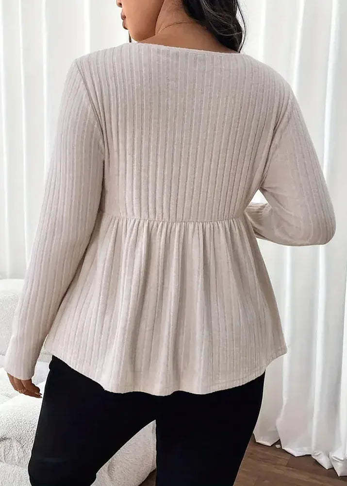 Person wearing a beige ribbed blouse with long sleeves against a white curtain background