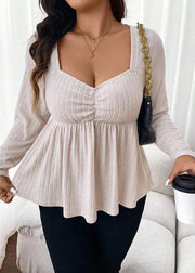 Woman wearing a beige long-sleeve top and black pants, holding a coffee cup.