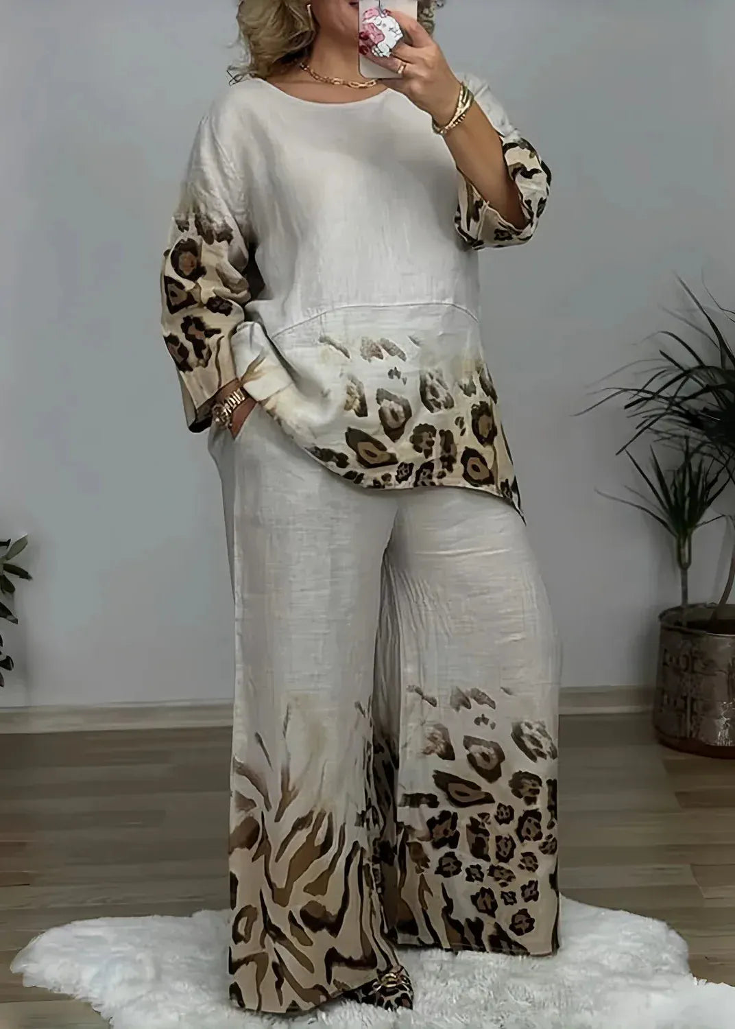 Person wearing a white outfit with leopard print sleeves and pants in a room with plants.