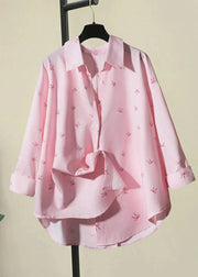 Pink blouse with small patterns on a hanger against a light green background