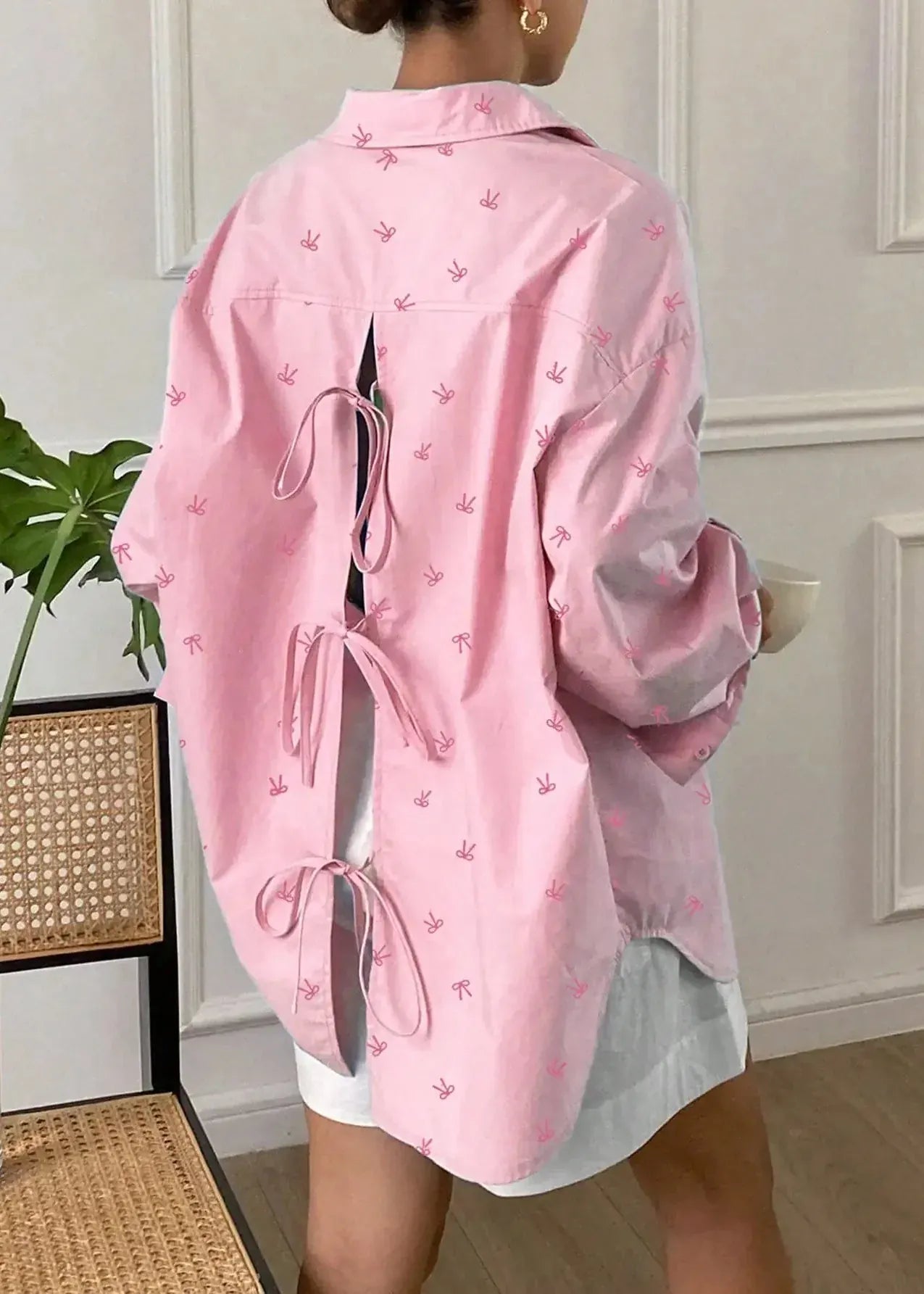 Person wearing a pink jacket with small patterns in a room with a plant and chair.