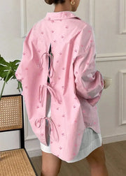 Person wearing a pink jacket with small patterns in a room with a plant and chair.