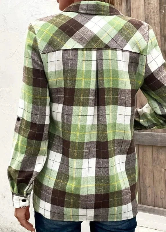 Green and brown plaid shirt worn by a person, with a wooden background.