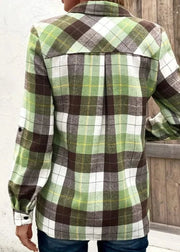 Green and brown plaid shirt worn by a person, with a wooden background.