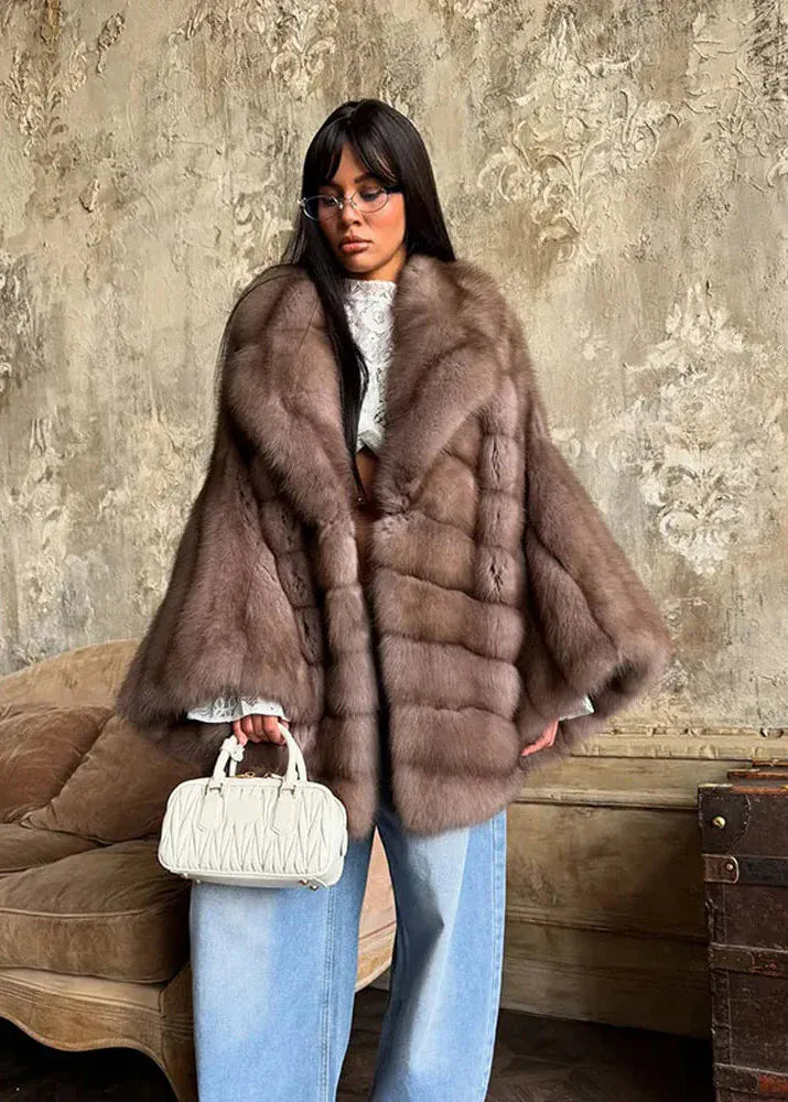 Woman wearing a fur coat holding a handbag against a textured wall.
