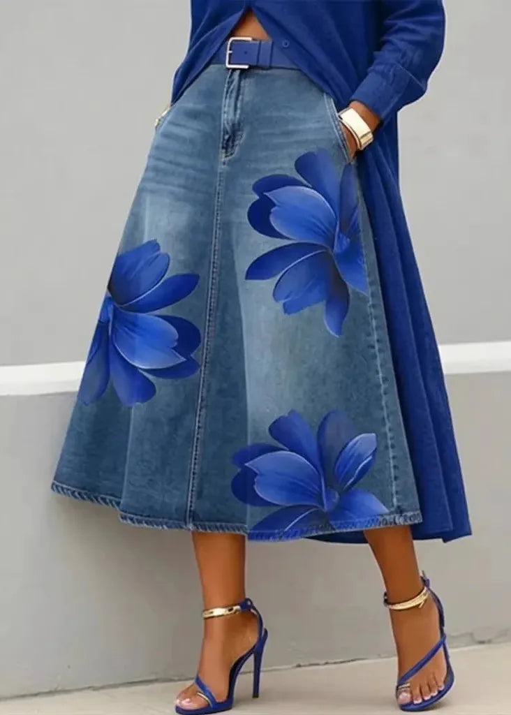 Person wearing a blue denim skirt with floral patterns against a gray background