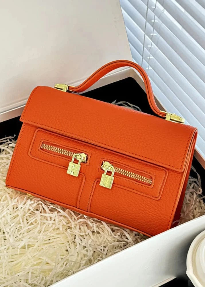 Orange handbag with gold zippers on a white surface
