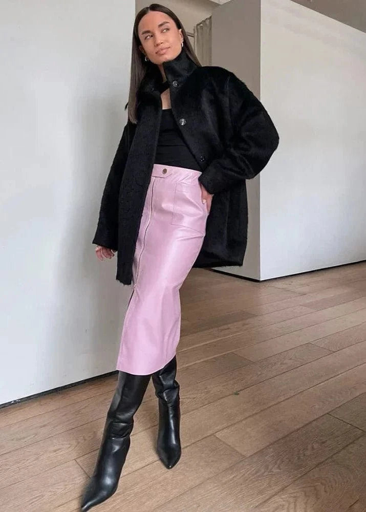 Person wearing a black coat, black top, pink pants, and black boots in a minimal indoor setting.