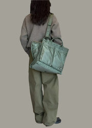 Person holding a green tote bag in an indoor setting with a black wall and white curtains.