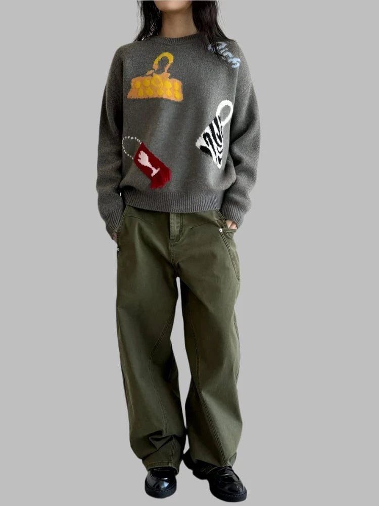 Person wearing a gray sweater with colorful designs and green pants in a room with white walls and wooden floor.