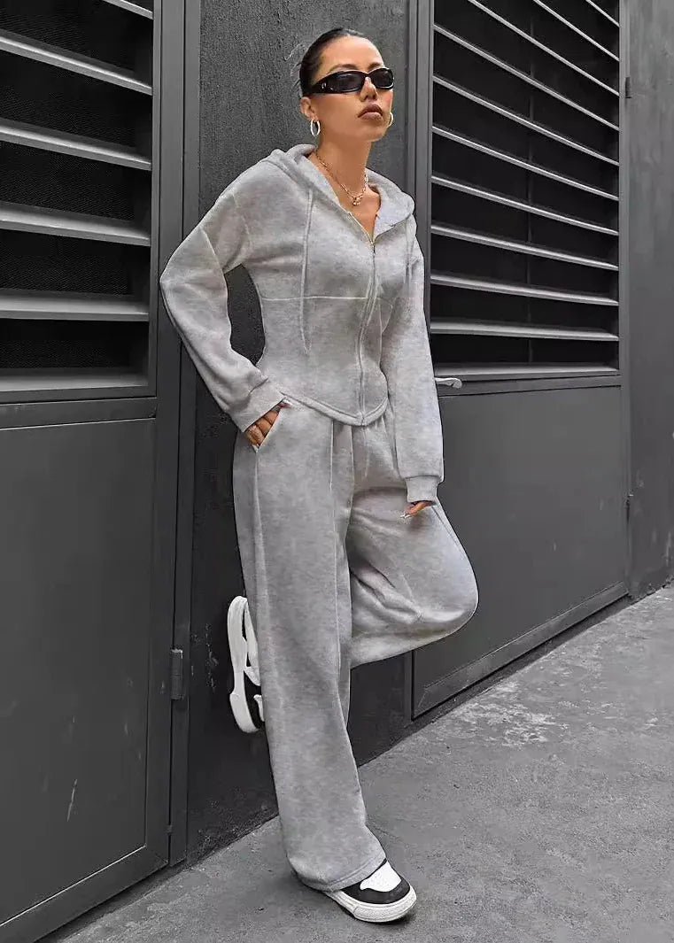 Person wearing a gray tracksuit standing against a dark wall.