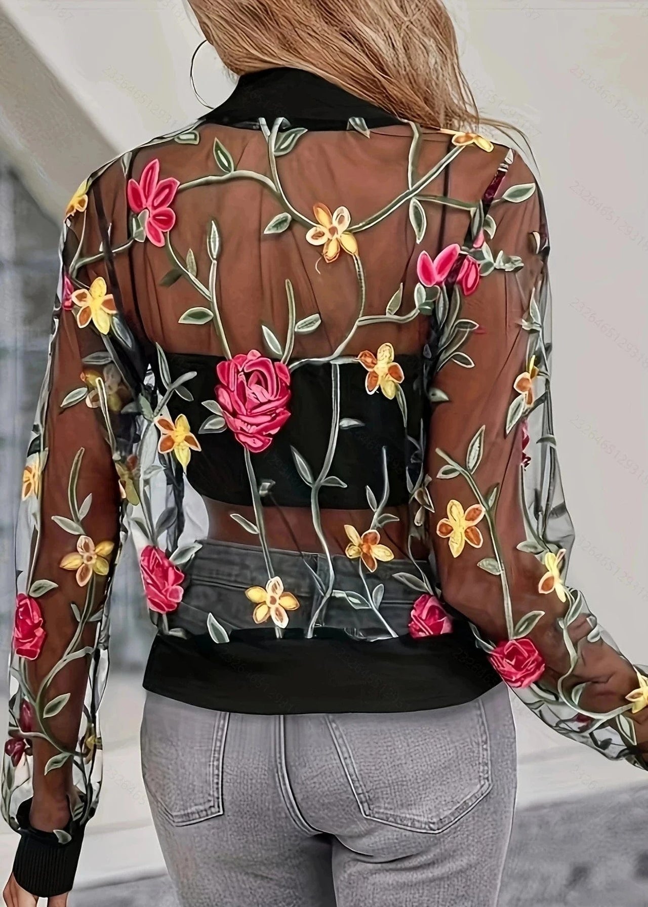 Person wearing a sheer jacket with floral embroidery in a blurred indoor setting