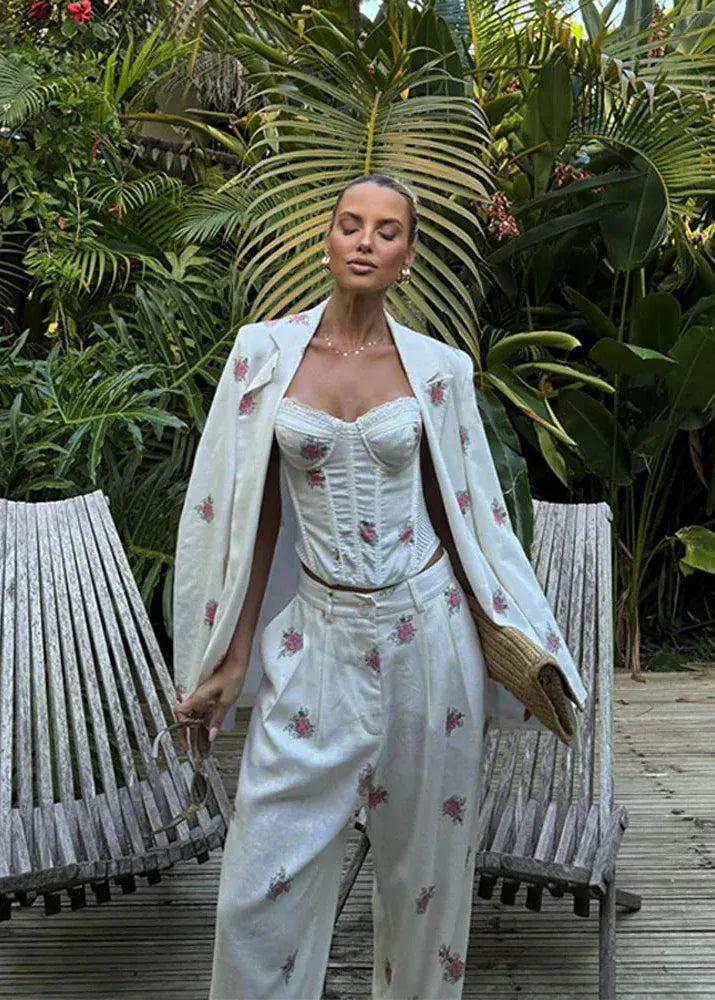 Woman in a white floral outfit standing in a tropical garden with wooden chairs.