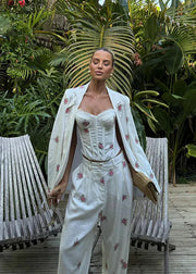 Woman in a white floral outfit standing in a tropical garden with wooden chairs.