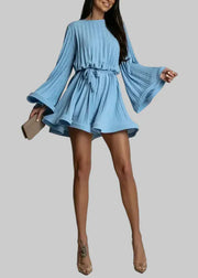 Woman wearing a light blue dress with bell sleeves on a plain background