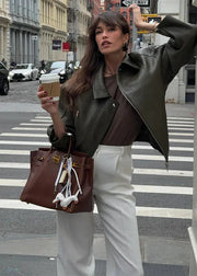 Woman crossing a street holding a coffee cup and brown handbag with earphones.