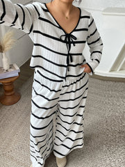 Person wearing a black and white striped outfit in a room with a white wall and wooden furniture.