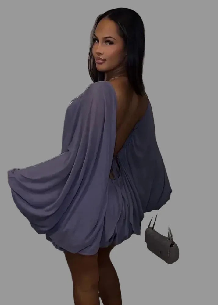 Woman in a flowing dress standing against a neutral wall.