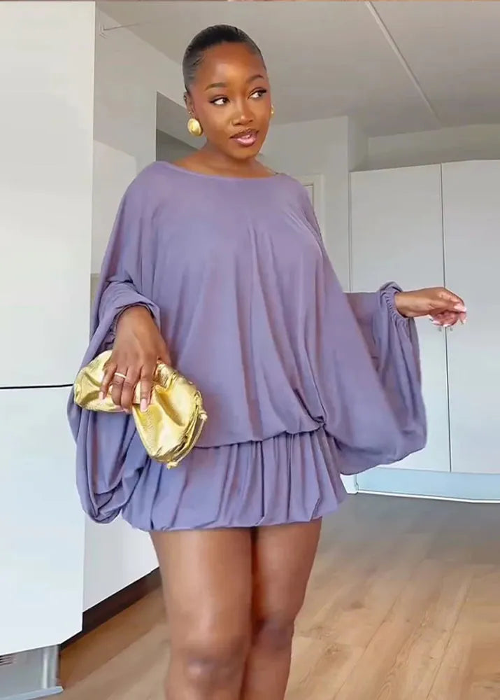 Woman wearing a light purple dress with balloon sleeves holding a gold clutch.