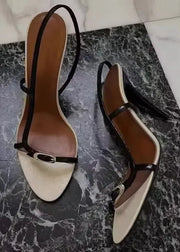 Pair of white high-heeled shoes with black straps on a marble surface