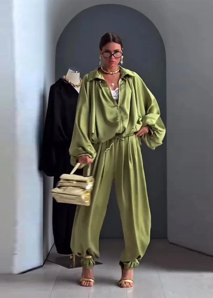 Woman in a green outfit holding a beige handbag in an indoor setting.