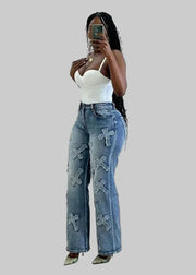 Woman taking a mirror selfie wearing a white top and blue jeans with cross designs.