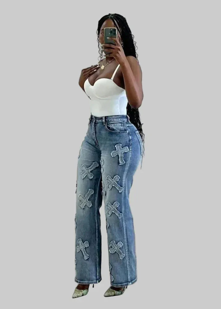 Woman taking a mirror selfie wearing a white top and blue jeans with cross designs.