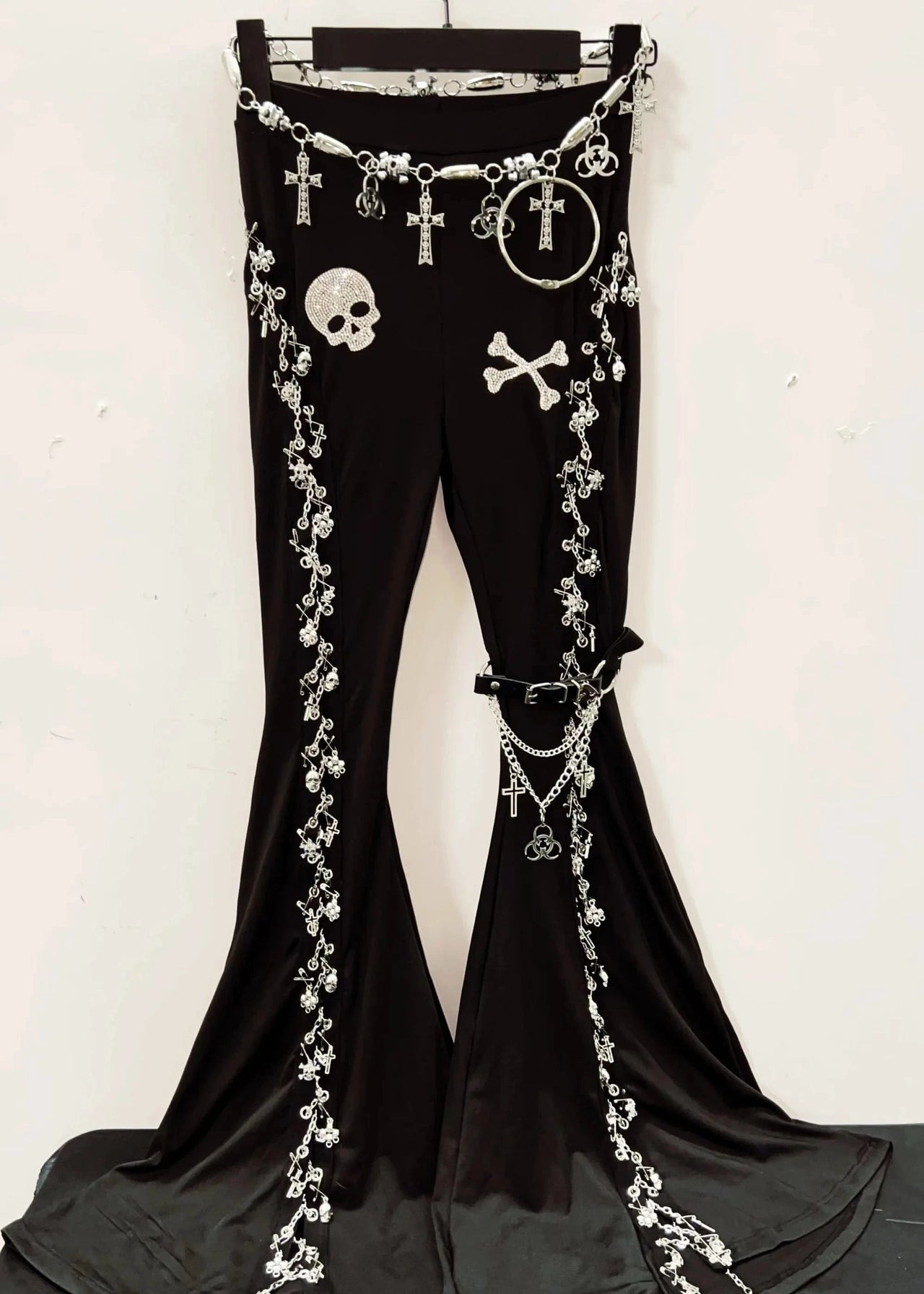 Black pants with decorative chains and skull designs on a hanger against a white background