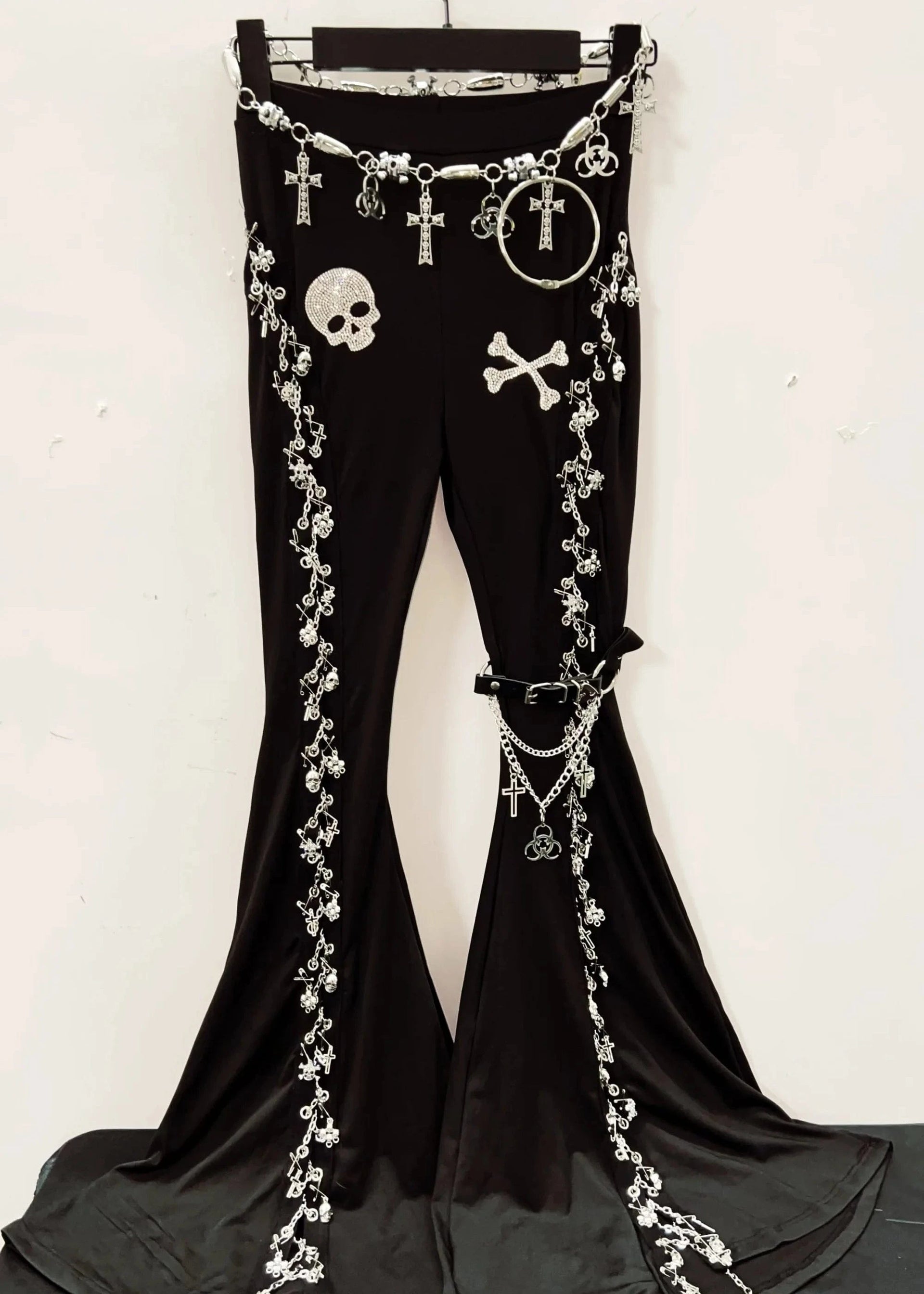 Black pants with decorative chains and skull designs on a hanger against a white background