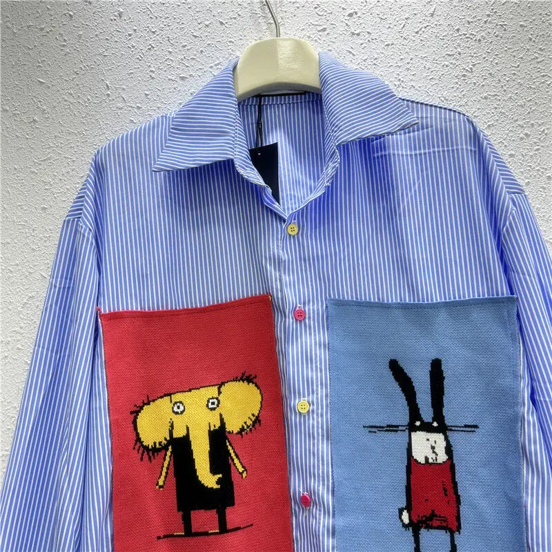 Blue striped shirt with red and blue pocket designs on a hanger against a gray wall.