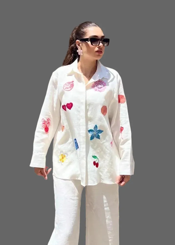 Woman wearing a white outfit with colorful patterns against a wooden background