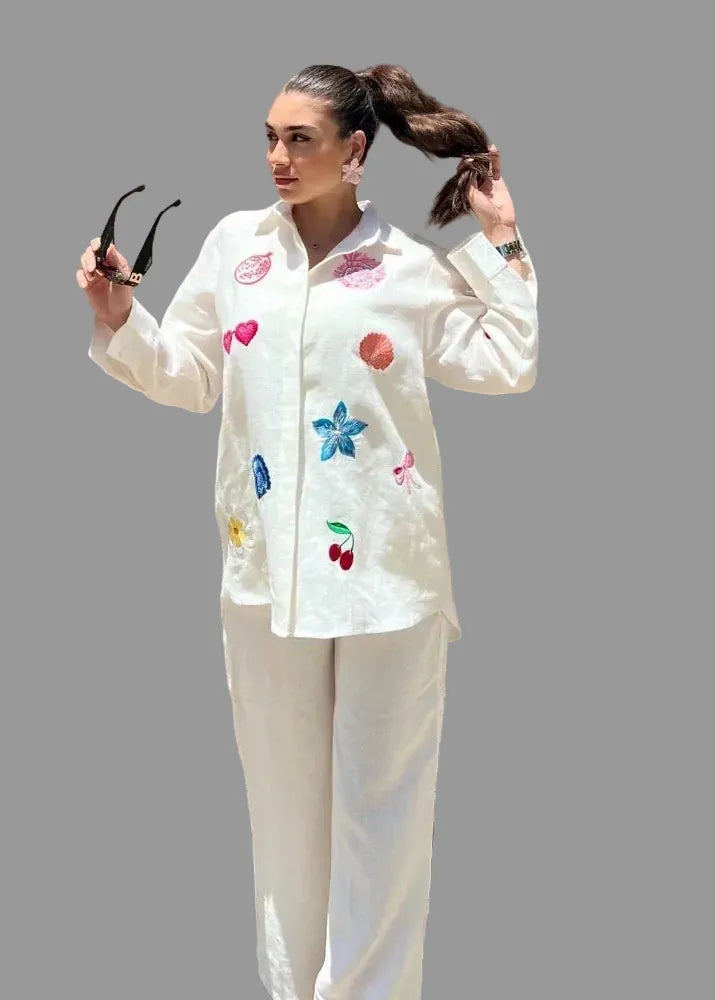 Woman wearing a white outfit with colorful floral and fruit patterns against a wooden background