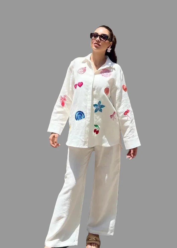 Woman wearing a white outfit with colorful designs against a wooden wall.