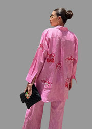 Woman wearing a pink embroidered outfit standing against a wooden wall, with 'MUCHENLOVE' branding visible.