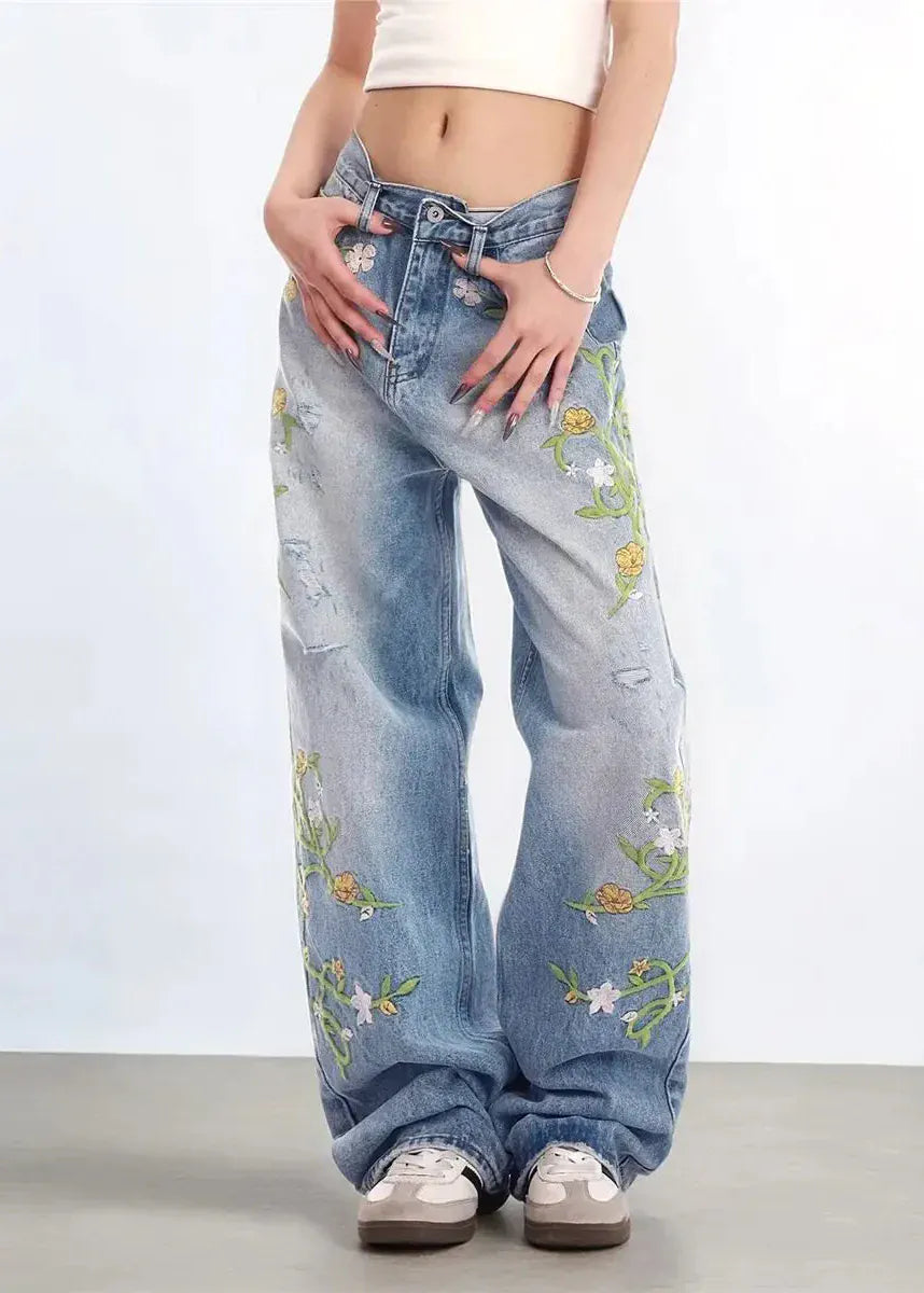 Person wearing floral embroidered jeans on a plain background