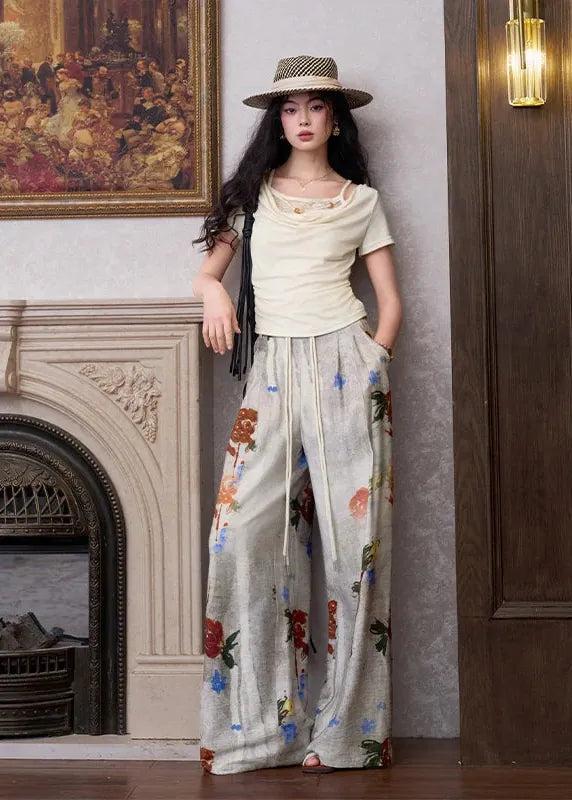 Woman in a stylish outfit with floral pants and a hat in an elegant room.
