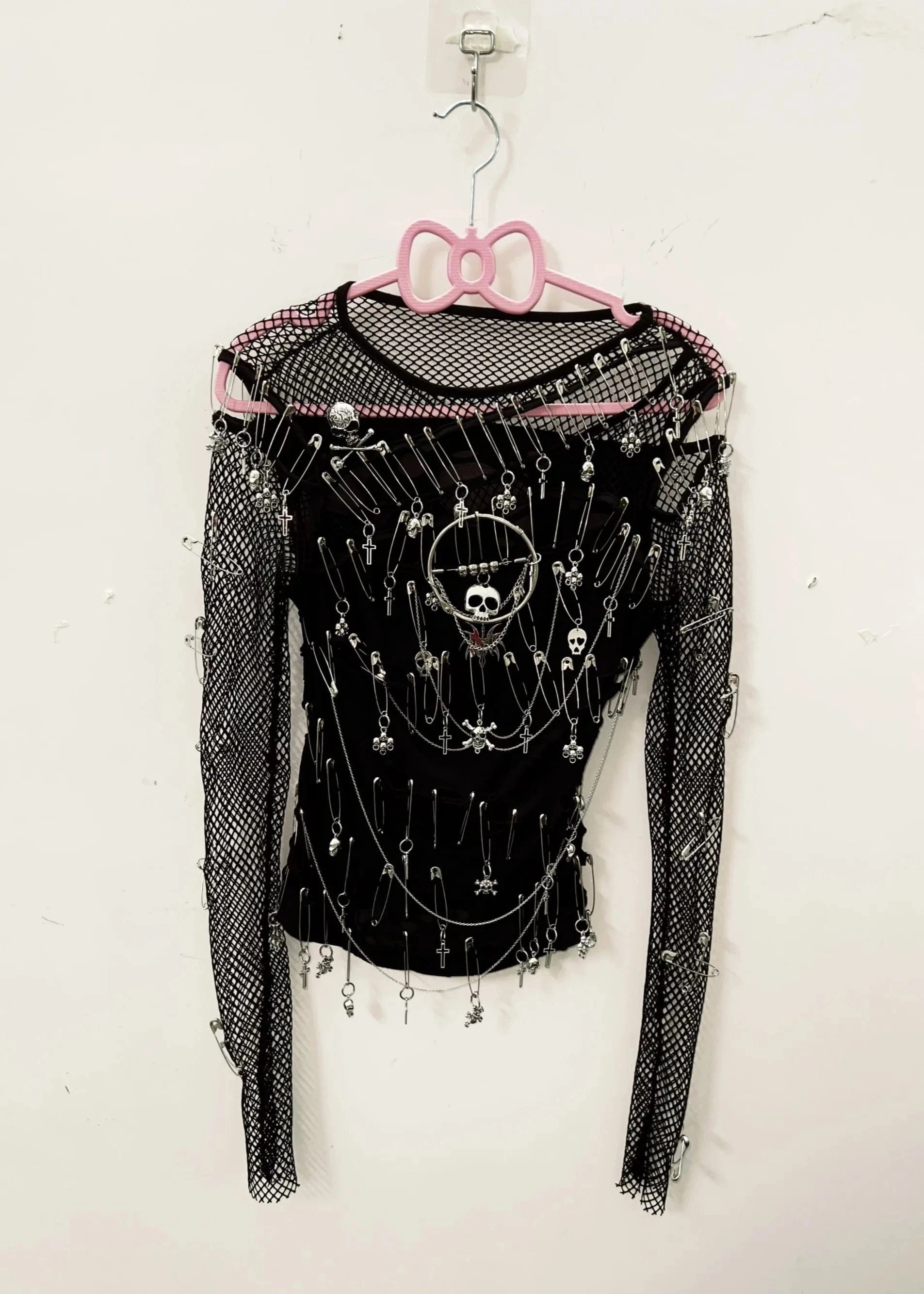 Black long-sleeve top with decorative elements on a pink hanger against a white background