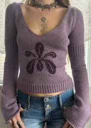 Person wearing a purple sweater with a black design, standing against a neutral background.