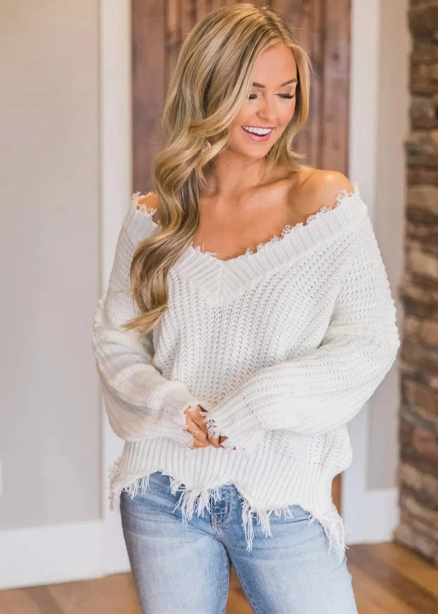 Woman wearing a white off-shoulder sweater and blue jeans indoors.