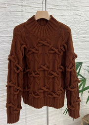 Brown cable knit sweater on a hanger against a textured white wall.