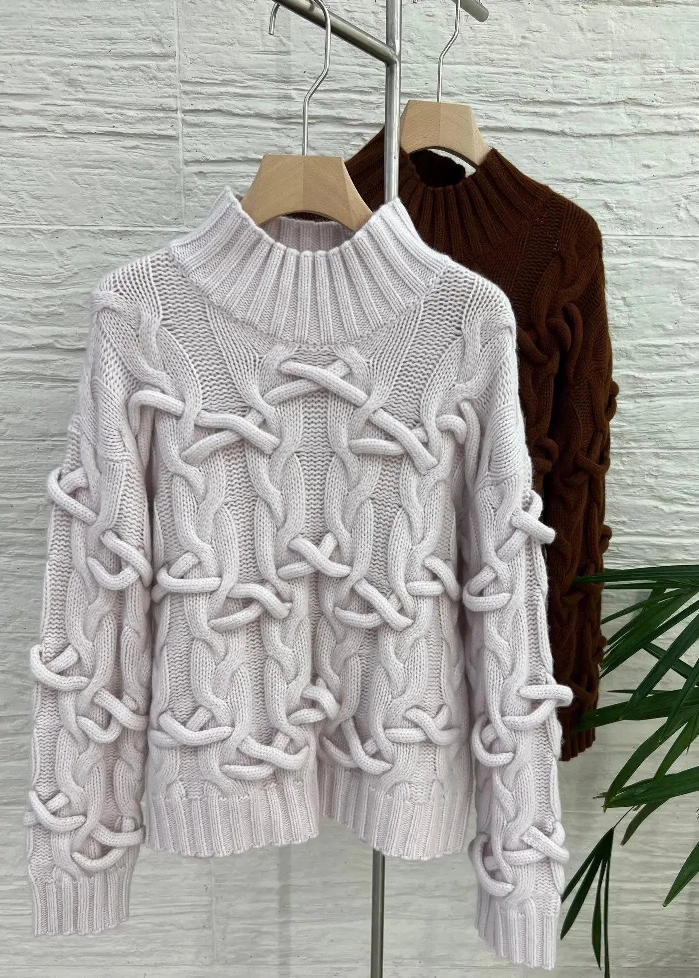 White cable knit sweater on a hanger against a textured wall.
