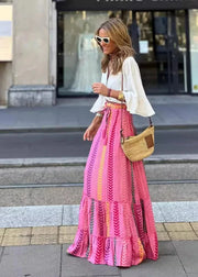 Woman in a pink dress with a white top and sunglasses, standing on a city street.