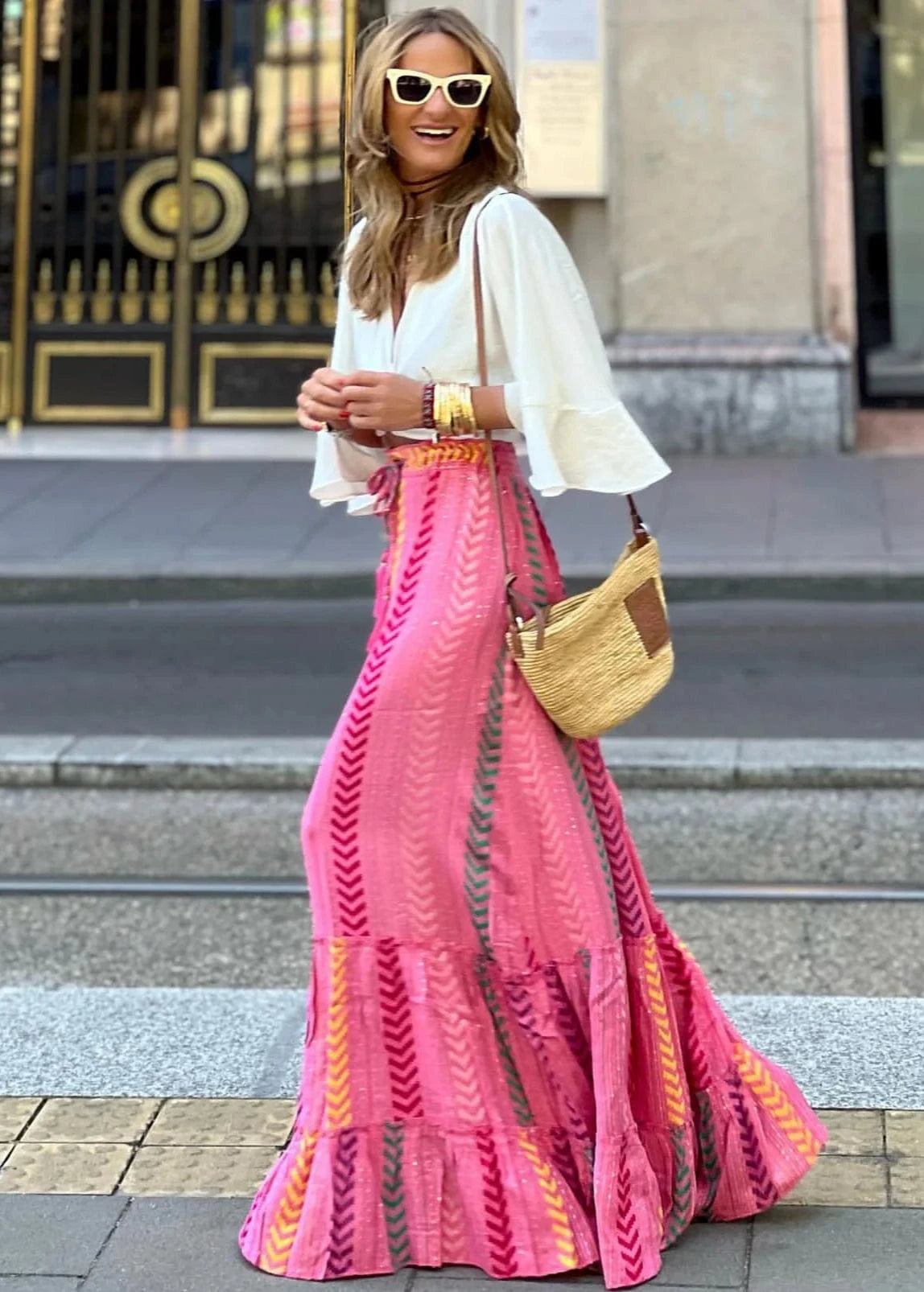Woman wearing a white top and pink skirt with yellow patterns, standing on a city street.