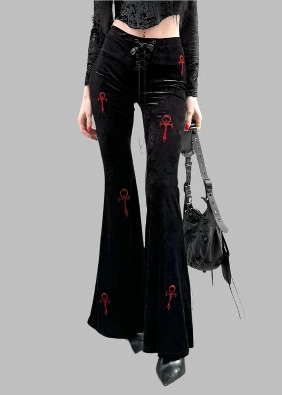 Person wearing black flared pants with red symbols, standing on a street.